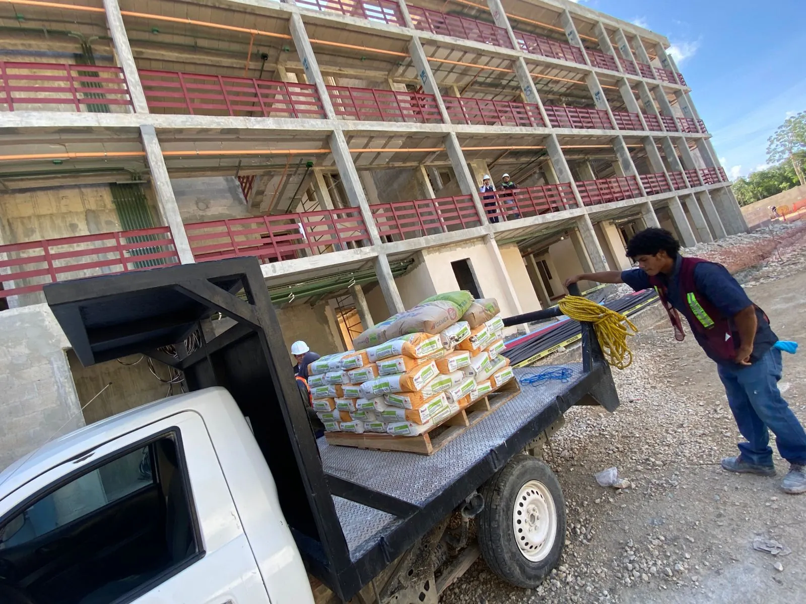Camioneta con una tarima de sacos junto a un edificio de cuatro niveles en obra