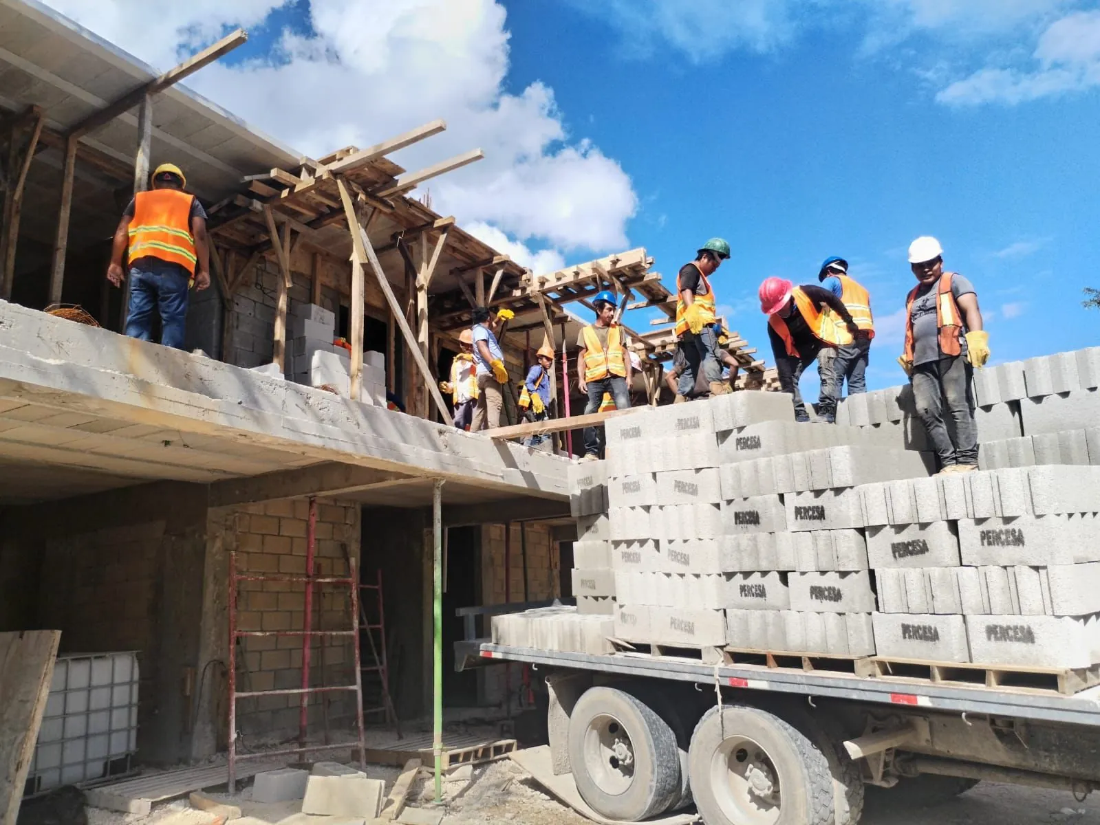 Trabajadores con casco descargando block de un camión en una obra de dos niveles