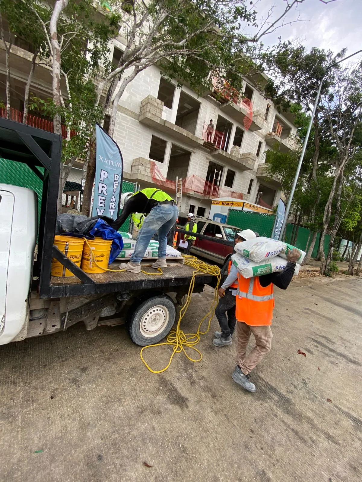 Trabajador con chaleco naranja cargando un saco desde una camioneta en obra